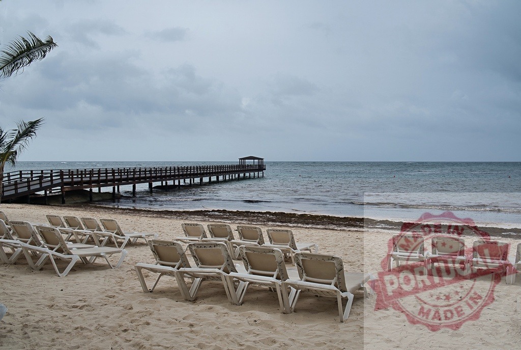 Empty beach chairs under cloudy sky overlooking Caribbean pier | Empty beach chairs lining a tropical resort beach with a pier stretching into the ocean - Realized with Pictrs.com