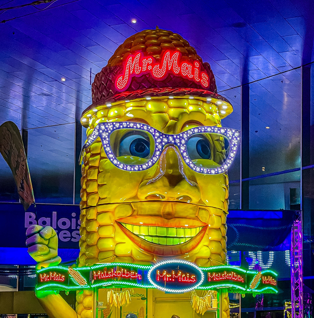 Basel Herbstmesse – Kultiger Mr. Mais Stand bei Nacht | Originelle Pop-Art Fotokunst aus Basel: Das leuchtende Gesicht von Mr. Mais auf der Basler Herbstmesse fängt die bunte, nostalgische Jahrmarkt-Atmosphäre perfekt ein. Mit seiner funkelnden LED-Brille und den knalligen Farben ist dieses Wandbild ein absoluter Gute-Laune-Garant und ein moderner Eyecatcher. Perfekt als hochwertiger Kunstdruck, Leinwand oder auf Acrylglas für ein kreatives Küchendesign oder moderne Wohnräume. - Realisiert mit Pictrs.com