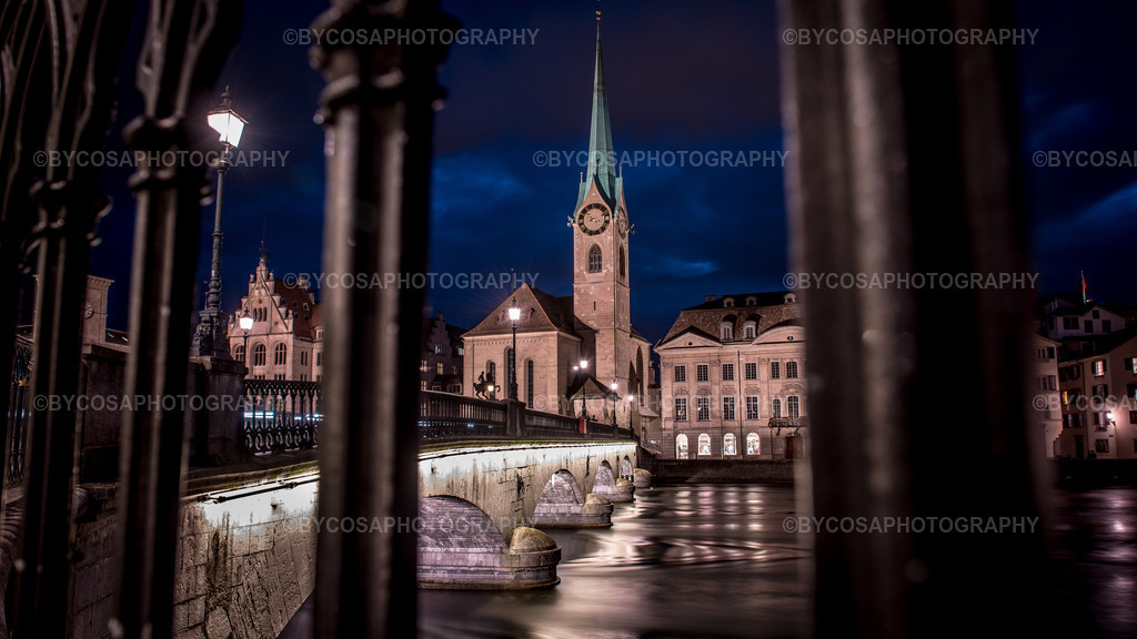 1 | Stimmungsvoller Nachtblick durch historische Arkaden auf das beleuchtete Fraumünster und die Münsterbrücke in der Zürcher Altstadt. Die Langzeitaufnahme zeigt die besondere Architektur und Atmosphäre Zürichs an der Limmat. Erhältlich als hochwertiger Fotoprint, Wandbild oder Fotoprodukt. - Realisiert mit Pictrs.com