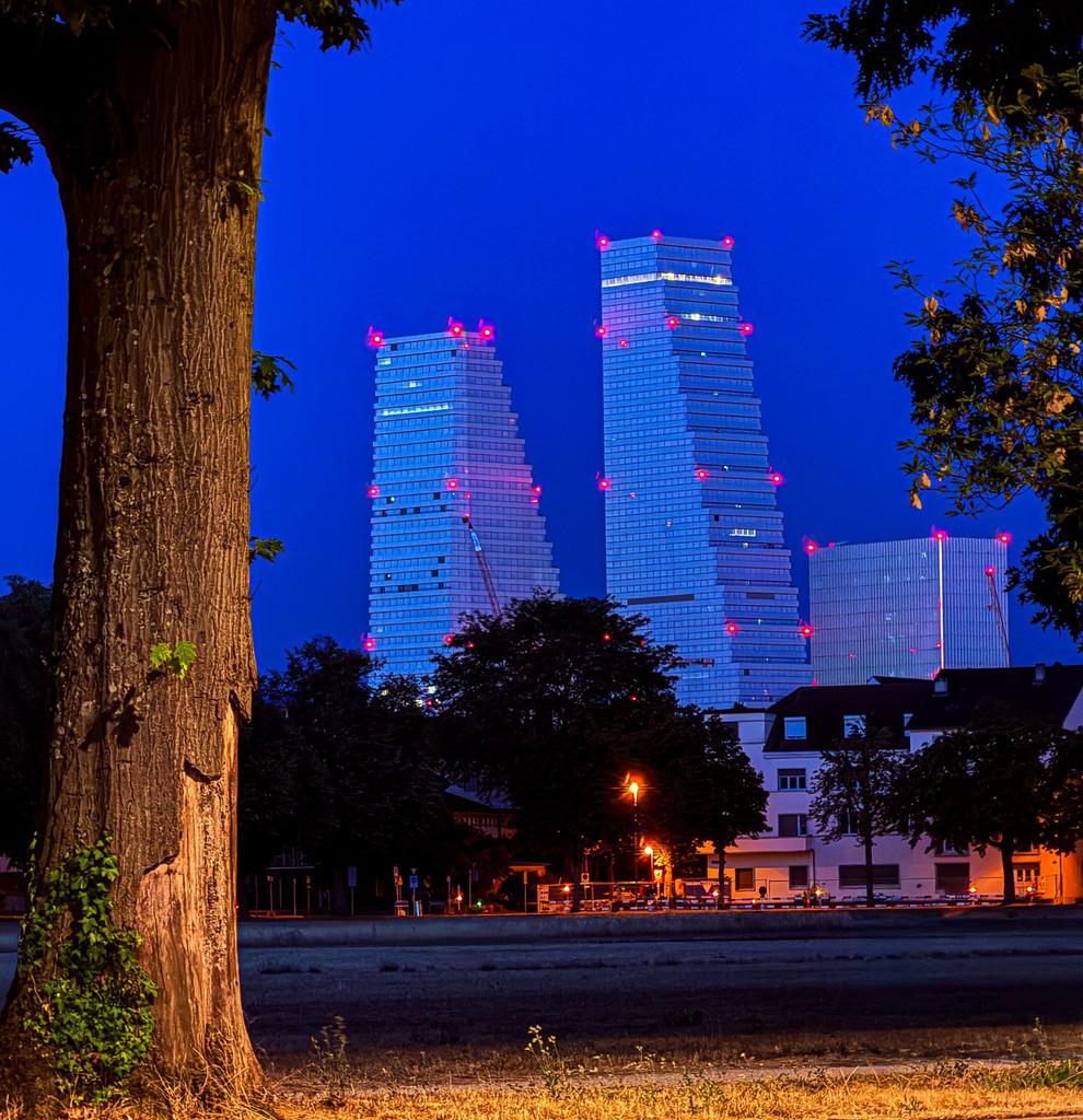 Wandbild Roche Towers Basel bei Nacht - Moderne Architektur | Dieses beeindruckende Architektur-Wandbild zeigt die ikonischen Roche Towers in Basel während der blauen Stunde. Die majestätische Symmetrie und die beleuchteten Fensterfronten der modernen Wolkenkratzer kontrastieren faszinierend mit dem tiefen, klaren Nachthimmel. Fotograf Robert Steinke fängt die urbane Dynamik und geometrische Perfektion der Schweizer Metropole in einer hochauflösenden Komposition ein. Ein absolutes Must-have für Liebhaber moderner Architektur, Urban-Design-Enthusiasten und alle, die eine stilvolle, kosmopolitische Atmosphäre in ihre Räume bringen möchten. Perfekt als großformatiger Premium-Kunstdruck auf Alu-Dibond, Leinwand oder hinter glänzendem Acrylglas für maximale Tiefenwirkung. - Realisiert mit Pictrs.com