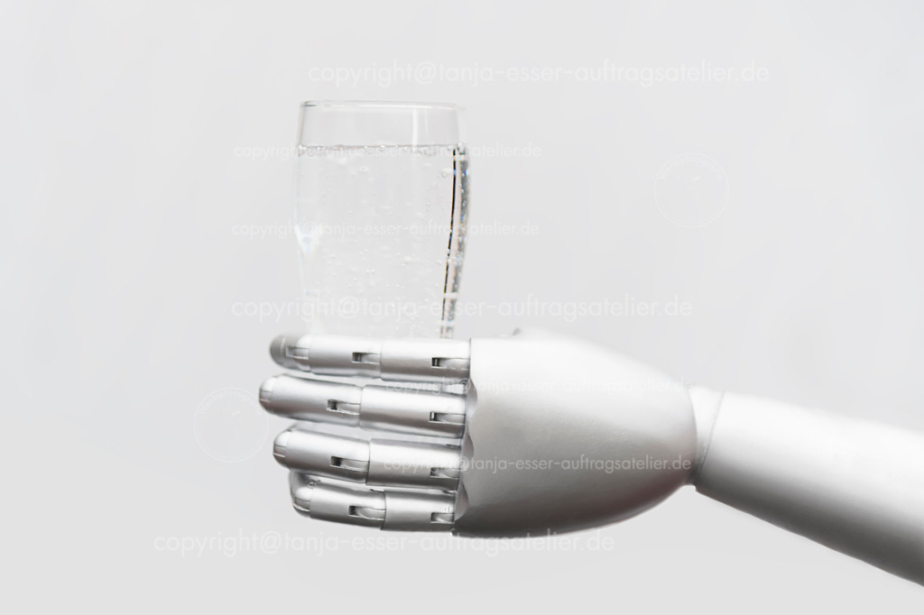 Robot holds a glass of water | Eine silberne Roboterhand hält ein Glas Mineralwasser. Isoliert gegen grauen Hintergrund.