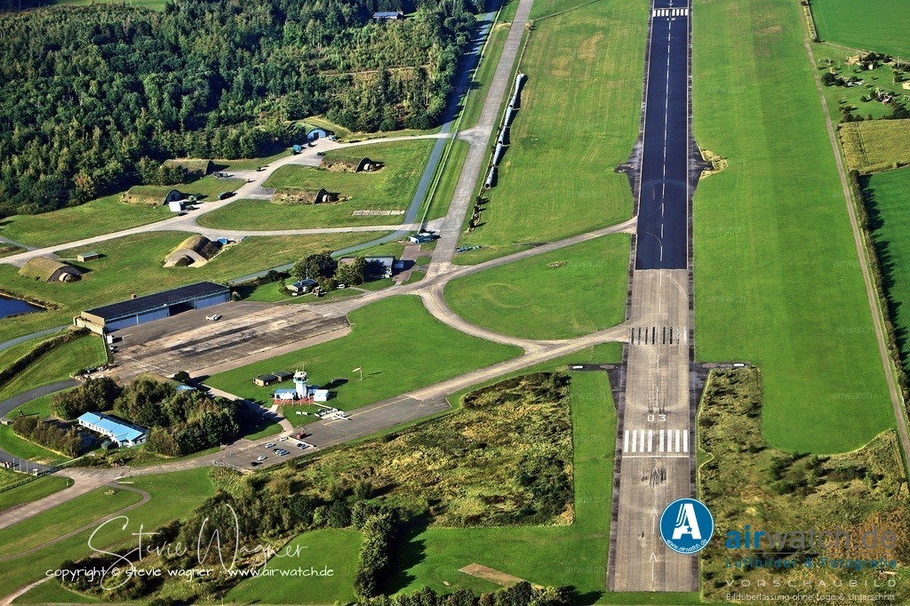 Luftbild Flughafen Husum-Schwesing - Die Nutzung des Fliegerhorsts durch die Bundeswehr endete 1993 | Das JaboG 41 wurde als letztes Geschwader auf den Alpha Jet umgerüstet, war aber im Zuge der Reduzierung der Streitkräfte nach der Wiedervereinigung Deutschlands das erste, das im Rahmen der Einnahme der Luftwaffenstruktur 4 aufgelöst wurde. Die Nutzung des Fliegerhorsts durch die Bundeswehr endete 1993. Der südwestliche Teil des ehemaligen Fliegerhorstes wurde in eine zivile Nutzung überführt und bildet heute den Standort des Flugplatzes Husum-Schwesing - Luftbild Position: Final / Endteil Piste 03 -