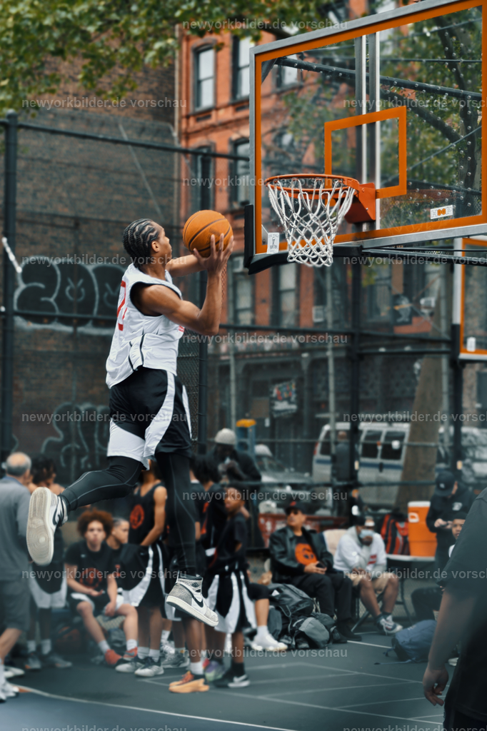 Spektakulärer Dunking auf dem West 4th Street Court – Streetball-Power in New York | Der West 4th Street Court ist ein Synonym für Streetball-Kultur in New York – und dieses Bild zeigt sie in ihrer intensivsten Form. Ein Spieler hebt ab, der Ball in der Hand, bereit für den kraftvollen Dunking. Die Szene ist voller Energie: gespannte Körper, der Asphalt unter den Füßen, die Rufe der Zuschauer im Hintergrund. Hier geht es nicht nur um Punkte, sondern um Ausdruck, Stil und Respekt. Streetball ist ein Lifestyle, der über den Sport hinausgeht – geprägt von Persönlichkeiten, Geschichten und einer Community, die sich auf diesem legendären Platz trifft. Der Moment des Dunkings ist pure Dynamik, eingefroren in einem Bild, das die Leidenschaft und Kreativität der Spieler sichtbar macht. Wer diesen Court kennt, weiß: Hier entstehen Legenden, hier lebt die Seele des Basketballs mitten in Manhattan.