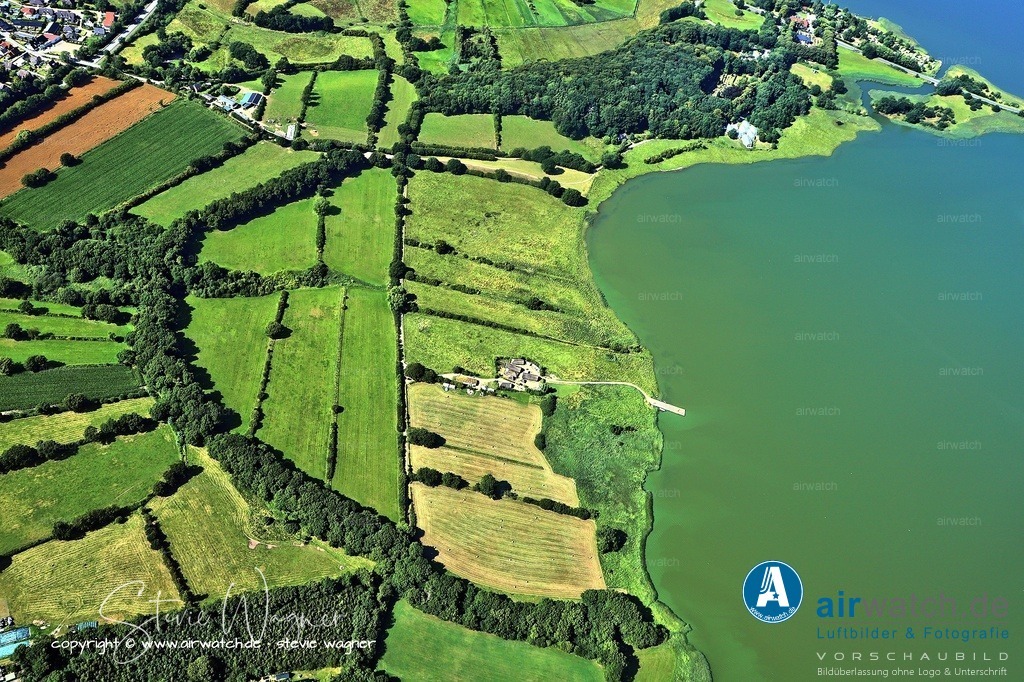 Haithabu - Befestigung und militärische Rolle - Luftbild | Zum Schutz vor Angriffen wurde Haithabu im 10.  Jahrhundert mit einem halbkreisförmigen Wall befestigt, der direkt an das Danewerk – eine große Grenzbefestigung zwischen Dänemark und dem Fränkischen Reich – anschloss.  Diese Verbindung machte die Stadt zum Kern eines strategischen Grenzkomplexes, der Handelsrouten und Herrschaftsgebiete kontrollierte.