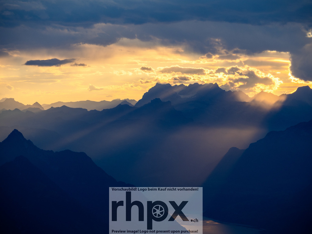 Lichtdurchflutete Gipfel | <p><strong>Licht. Weite. Magie.</strong></p><p>Dramatische Sonnenstrahlen durchbrechen die Wolkendecke und tauchen die gestaffelten Bergketten in ein atmosphärisches, goldenes Licht. Dieser Moment fängt die pure Erhabenheit der Alpen in einer einzigartigen Lichtstimmung ein.</p><p>Wähle unter "Produktauswahl" dein Wunschformat: Vom klassischen Wandbild über Puzzle & Tassen bis zum digitalen Download (z.B. als Handy-Hintergrund).</p> - Realisiert mit Pictrs.com