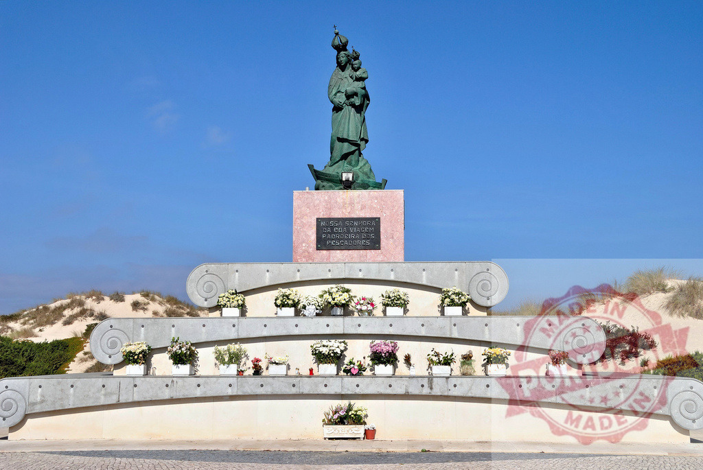 Nossa Senhora da Boa Viagem statue honoring fishermen in Peniche Portugal. Centro - Portugal | Our Lady of Good Voyage monument with flowers and sand dunes under a clear blue sky - Realized with Pictrs.com