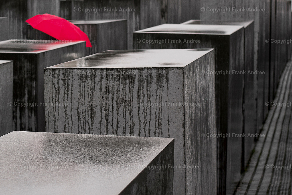 Gedenken im Regen | Das Holocaust Mahnmal in Berlin an einem regnerischen Tag. Zwischen den Betonstelen ein einzelner roter Regenschirm. Straßenfotografie aus Berlin. - Realisiert mit Pictrs.com