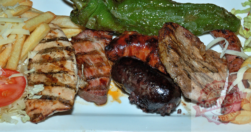 Assorted grilled meat platter with fries and vegetables | Mixed grill offering different meats, Spanish chorizo, and blood sausage with french fries and pepper - Realized with Pictrs.com