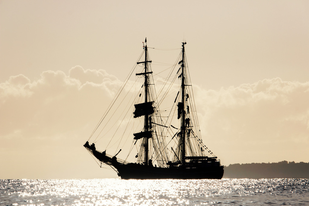 Erwachen auf See: Maritimer Morgenglanz | Ein Moment voller Fokus und spätsommerlicher Klarheit. Dieses Wandbild fängt die besondere Lichtstimmung eines Septembermorgens auf der Ostsee ein, wenn die tiefstehende Sonne die Masten eines Traditionsseglers in ein silbrig-goldenes Licht taucht. Bei genauem Hinsehen zeigt sich das lebendige Erbe der Seefahrt: Hoch oben in der Takelage erkennt man im Gegenlicht die Silhouetten der Besatzung bei der täglichen Arbeit. Das Motiv vereint die friedliche Weite des Meeres mit dem unverfälschten Handwerk an Bord. Ein zeitloses Kunstwerk, das die Ruhe und die klare, frische Energie eines neuen Tages an der Küste perfekt in Ihr Zuhause bringt. - Realisiert mit Pictrs.com