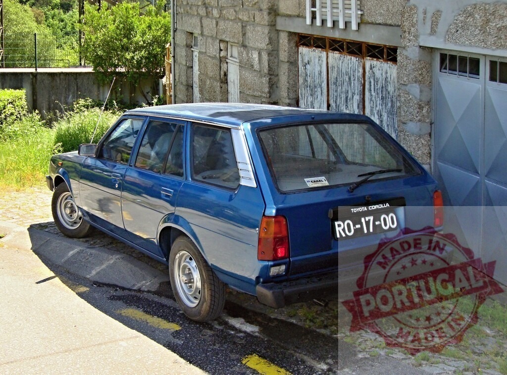 Blue Toyota Corolla KE70 station wagon parked near stone wall in Portugal | Classic blue Toyota Corolla KE70 station wagon parked on a cobblestone street near a stone wall and garage door, showcasing vintage automotive design - Realized with Pictrs.com
