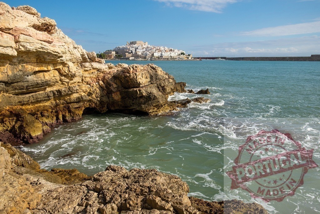 Peñíscola cityscape rising above the sea, seen from a rocky beach in Spain | Waves crashing on the rocks of a beach with the cityscape of Peñíscola in the background - Realized with Pictrs.com