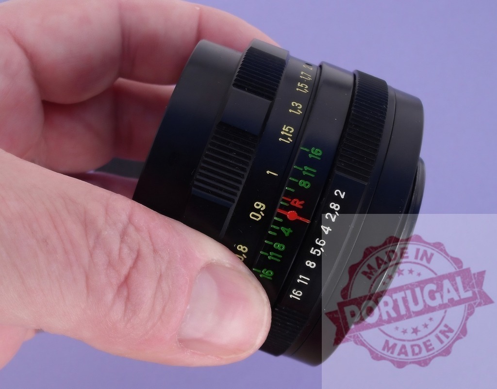 Photographer holding old camera lens adjusting settings | Hand holding vintage photographic lens with focus and aperture rings on lavender background - Realisiert mit Pictrs.com