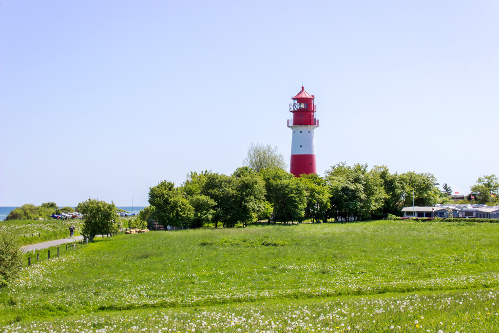 Wandbild: Leuchtturm in Falshöft im Frühling | Dieses Wandbild im Querformat zeigt einen der schönsten Leuchttürme in an der Ostseeküste in Falshöft. Im Vordergrund befindet sich eine grüne Wiese und direkt vor dem Leuchtturm befinden sich zahlreiche Bäume. Holen Sie sich dieses idyllische Wandbild nach Hause in Ihr Wohnzimmer, Küche, Schlafzimmer oder in Ihre Ferienwohnung, Büro, den Arbeitsplatz oder Ihre Praxis. Es ist als Leinwand, als Acrylglas/Glasbild und Aluminium-Platte in vielen Abmessungen erhältlich. - Realisiert mit Pictrs.com