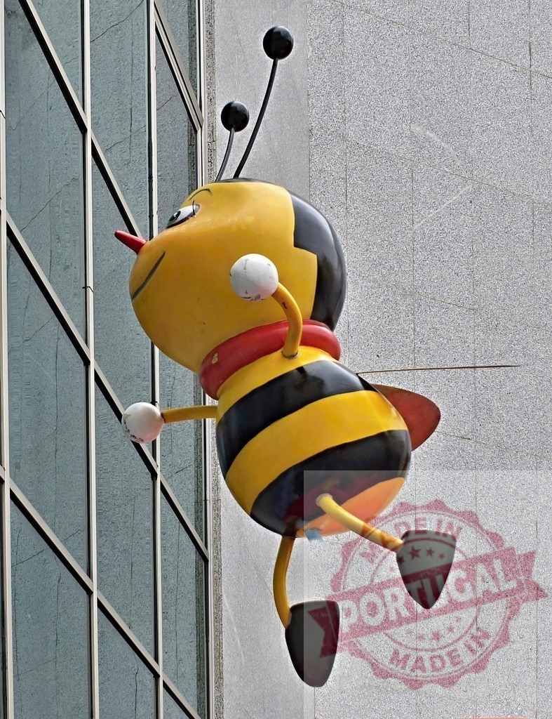 Cartoon bee mascot sculpture attached to building wall | Yellow and black cartoon bee sculpture decorating a modern urban building facade - Realisiert mit Pictrs.com