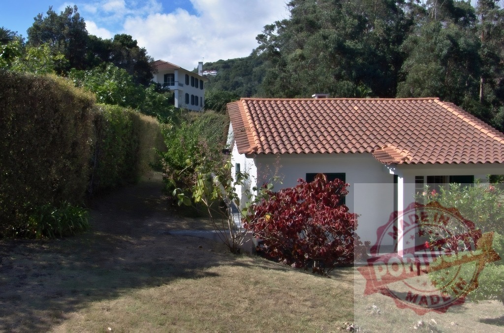 White holiday home with terracotta roof enjoying lush garden | White house with red-tiled roof and surrounding green vegetation under a blue sky - Realized with Pictrs.com