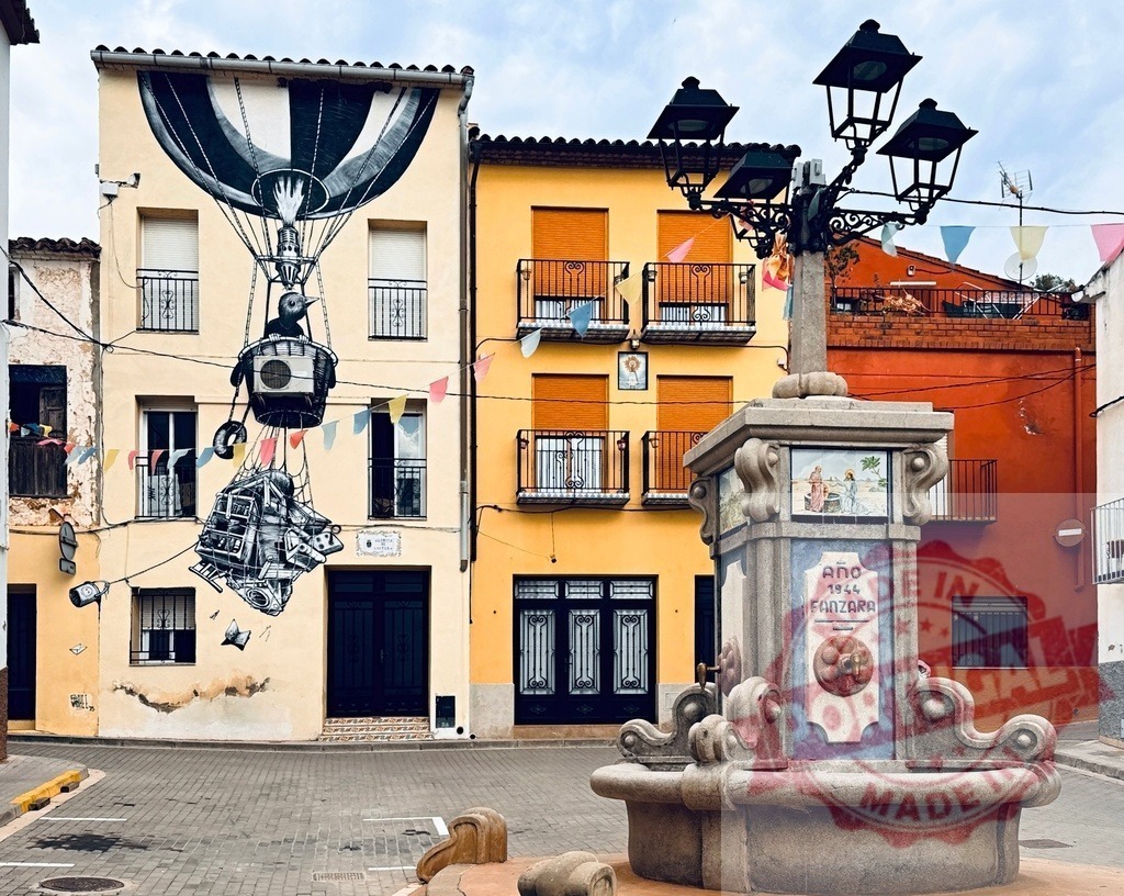 Fanzara village square displaying street art and fountain | Fanzara village displaying vibrant street art mural of a hot air balloon and an ancient fountain - Realisiert mit Pictrs.com