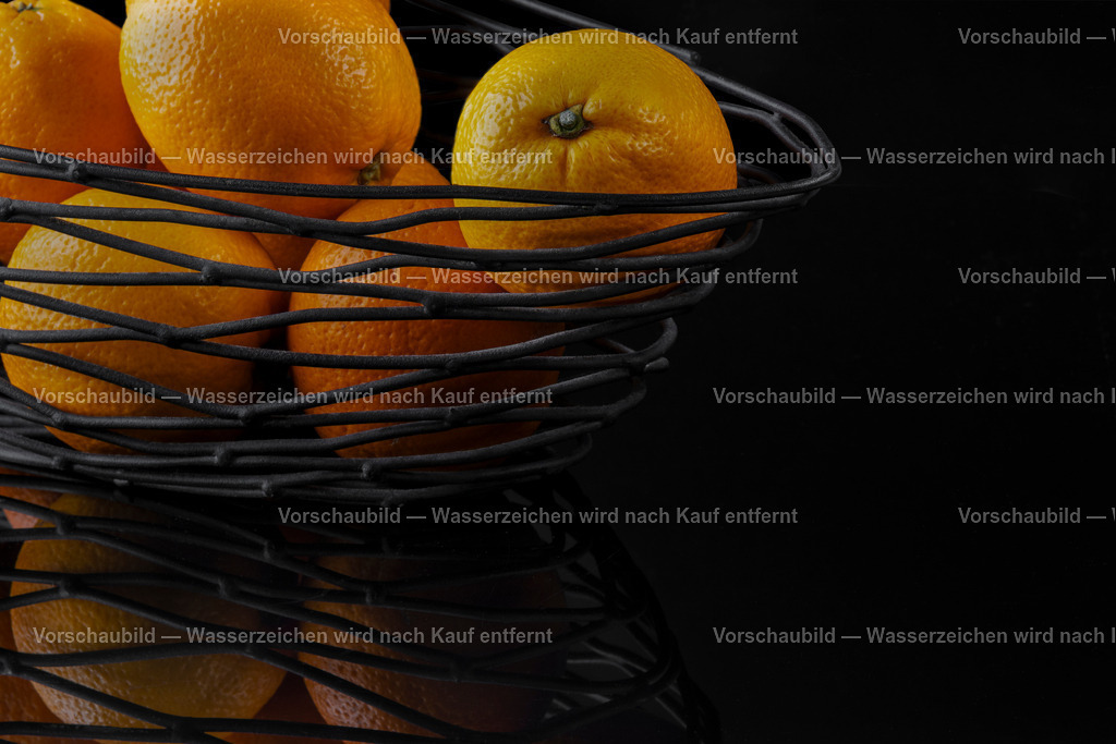 ein schwarzer Drahtkorb mit frischen Orangen auf spiegelnden, schwarzen Untergrund | ein schwarzer Drahtkorb mit frischen Orangen auf spiegelnden, schwarzen Untergrund. - Realisiert mit Pictrs.com