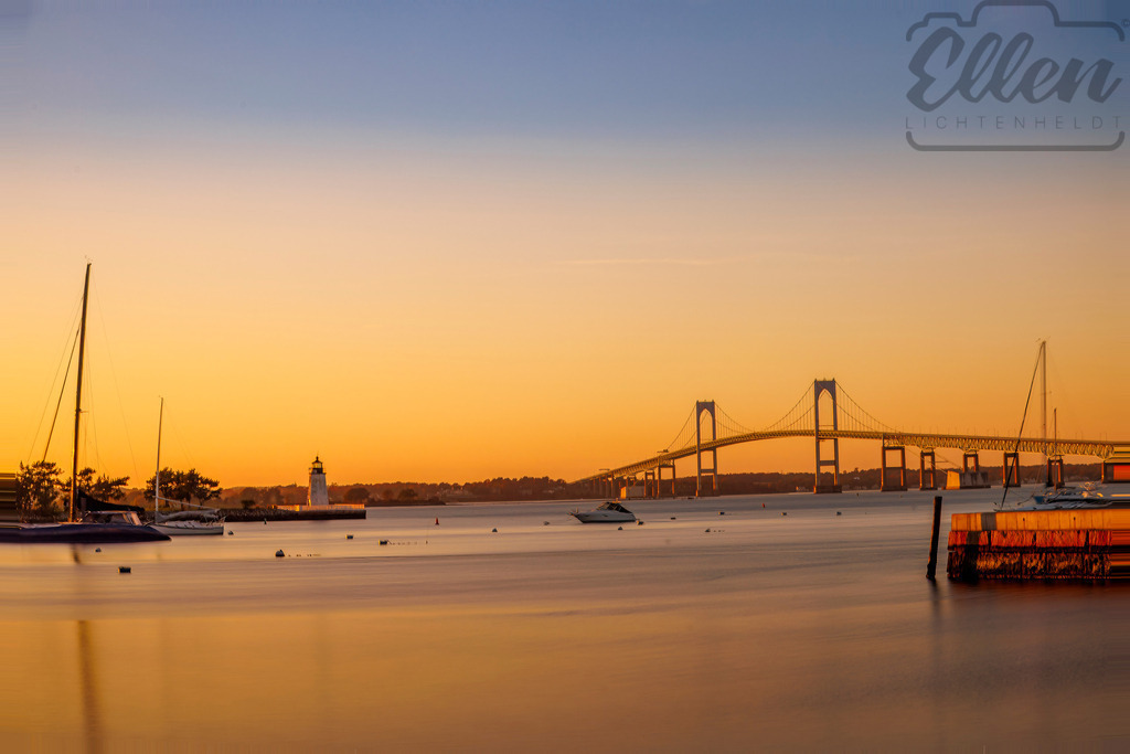 Harbour Glow | As the sun sets over Newport, the sky turns to gold. The calm water mirrors the light of the fading day, while boats and the bridge rest in perfect harmony — a moment of peace by the sea. - Realisiert mit Pictrs.com