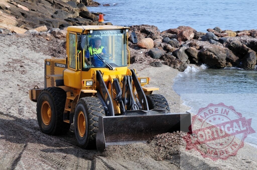 Volvo bulldozer cleaning beach removing seaweed | Yellow Volvo bulldozer removing seaweed from a sandy beach, improving coastal environment - Realized with Pictrs.com