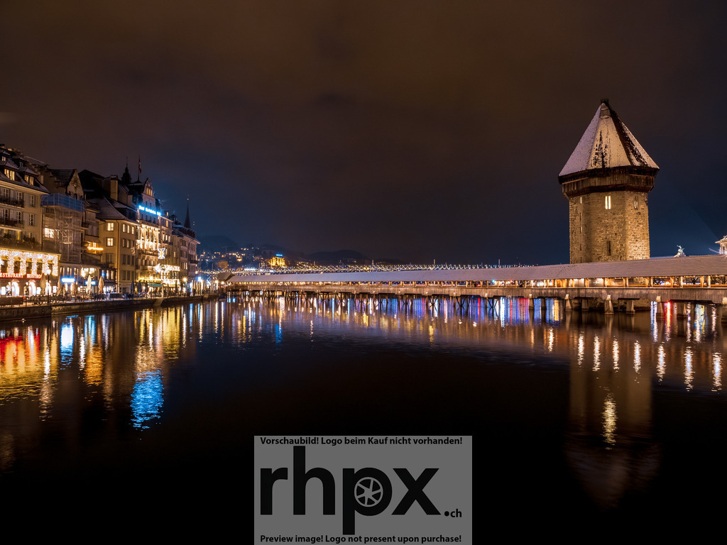Kapellbrücke bei Nacht | <p><strong>Licht. Reflexion. Wahrzeichen.</strong></p><p>Die beleuchtete Kapellbrücke ruht still über dem dunklen Wasser der Reuss. Die Lichter der Stadt und der schneebedeckte Wasserturm erschaffen eine unvergessliche Atmosphäre in dieser Winternacht.</p><p>Wähle unter "Produktauswahl" dein Wunschformat: Vom klassischen Wandbild über Puzzle & Tassen bis zum digitalen Download (z.B. als Handy-Hintergrund).</p> - Realisiert mit Pictrs.com