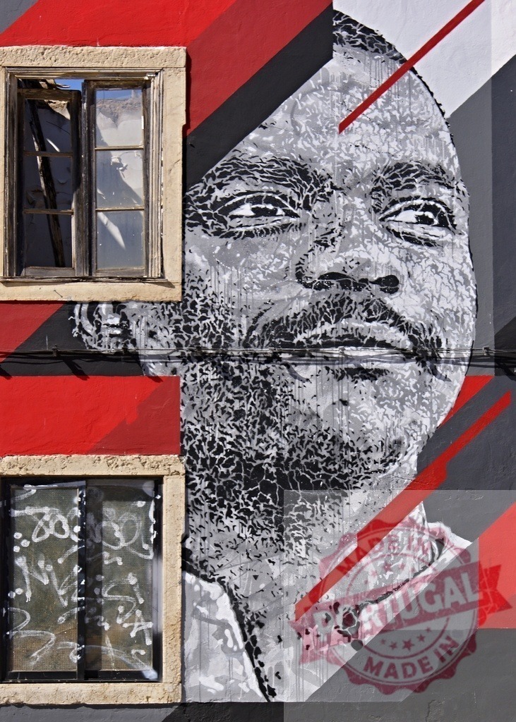 Vhils street art portrait on urban wall in Lisbon | Vhils street art portrait covering a building wall with windows, featuring geometric shapes and red accents - Realisiert mit Pictrs.com