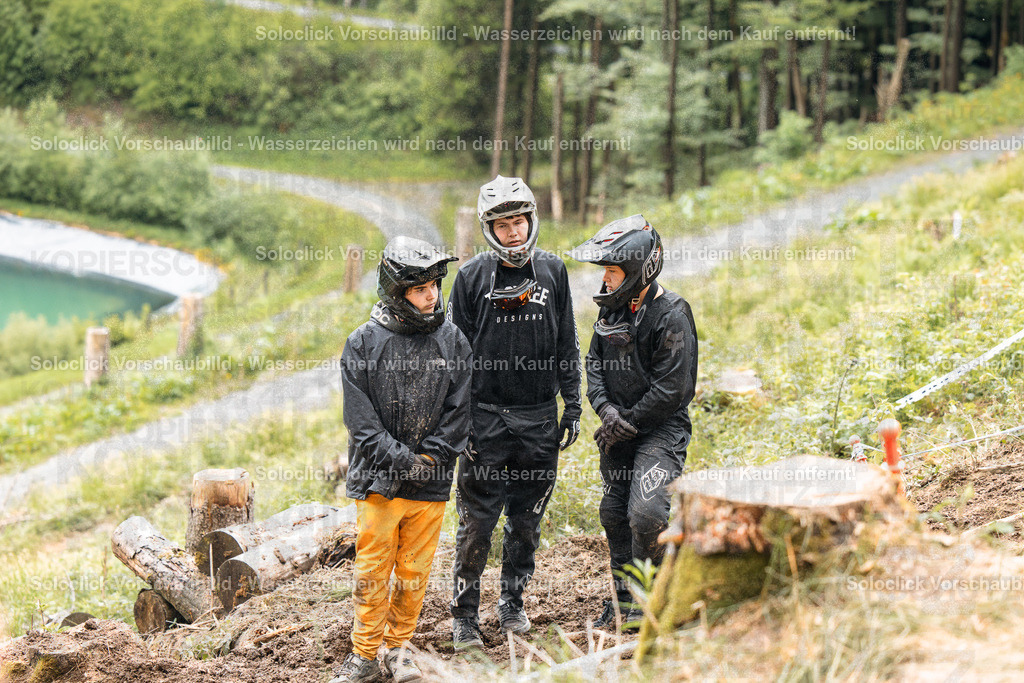 Mountainbiker in der Natur | Drei Mountainbiker stehen in einem bewaldeten Gebiet, während es regnet. Sie tragen alle Schutzkleidung, darunter Helme, Brillen und Regenkleidung. Die Szene vermittelt eine Atmosphäre der Konzentration und Vorbereitung auf eine bevorstehende Fahrt. - Realisiert mit Pictrs.com