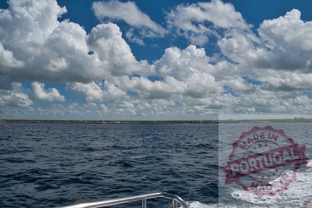 Navigating ocean waves under cloudy blue sky | Yacht sailing on the ocean with a coastline in the distance under a blue sky with clouds - Realisiert mit Pictrs.com