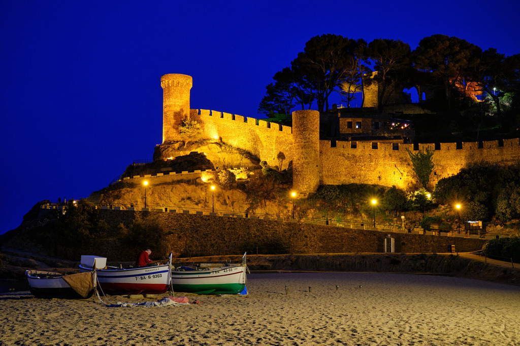 Blick über den Strand auf die Vila Vella im Abendlicht | Tossa de Mare, Frankreich - May 13, 2024: Blick über den Strand auf die Vila Vella im Abendlicht und Booten im Vordergrund. - Realisiert mit Pictrs.com