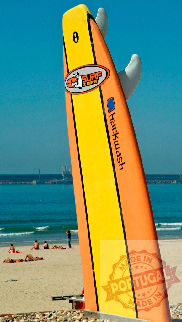 Surfboard standing on beach with sunbathers enjoying ocean | Colorful surfboard on the beach with people relaxing and sunbathing by the sea - Realisiert mit Pictrs.com