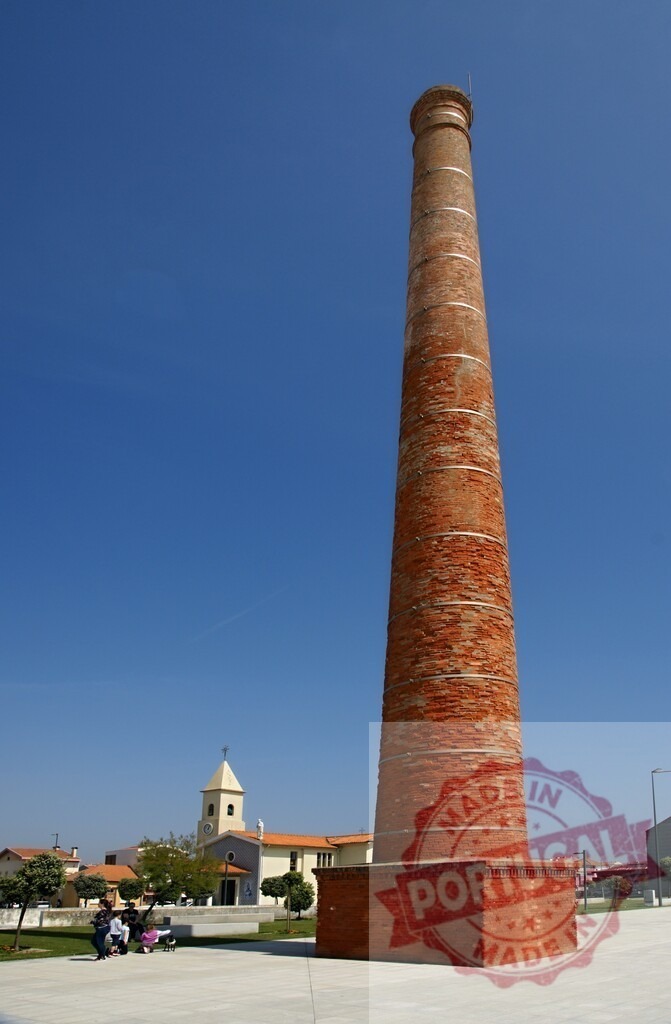 Old industrial chimney standing tall near a church | Tall brick chimney from an old factory building in a town square with a church - Realized with Pictrs.com