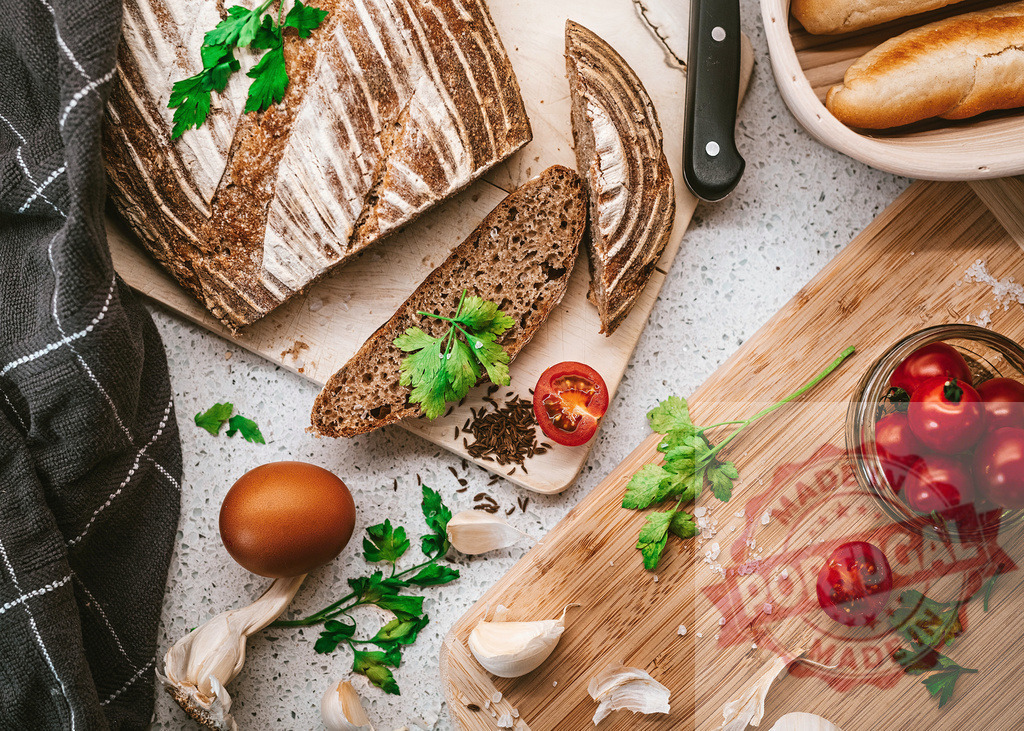Slicing rustic bread with fresh ingredients for a healthy breakfast | Sourdough bread, tomatoes, garlic, egg, and herbs preparing a wholesome breakfast - Realisiert mit Pictrs.com