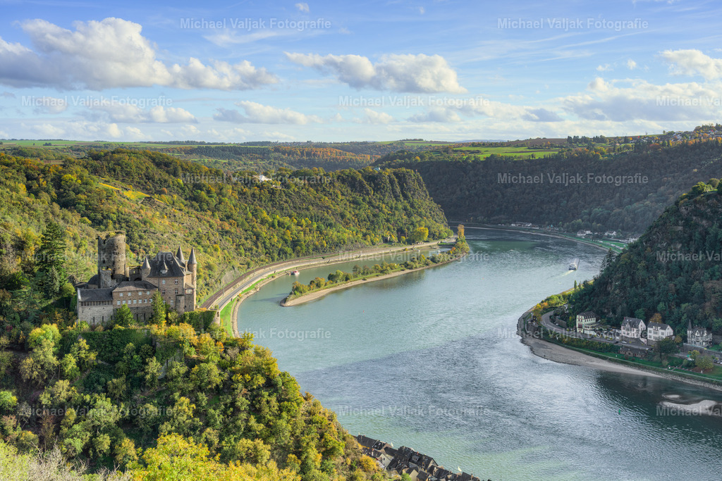 Burg Katz, Loreley und die Rheinschleife | Ein goldener Herbstnachmittag taucht das Rheintal in warmes Licht. Auf dem Foto thront die majestätische Burg Katz hoch über dem Fluss, ihre mittelalterlichen Mauern von buntem Laub umrahmt. Die Rheinschleife windet sich elegant durch das Tal, als wolle sie die Schönheit der Landschaft betonen. In der Ferne erhebt sich die sagenumwobene Loreley – ein Felsen, der Geschichten von Sehnsucht und Gefahr erzählt.Die Szenerie wirkt wie gemalt: sanfte Hügel, leuchtende Wälder und das ruhige Glitzern des Rheins. Es ist ein Moment der Stille und Erhabenheit, in dem Natur und Geschichte miteinander verschmelzen. Ein perfekter Augenblick, um innezuhalten und die Magie des Herbstes zu spüren. - Realisiert mit Pictrs.com