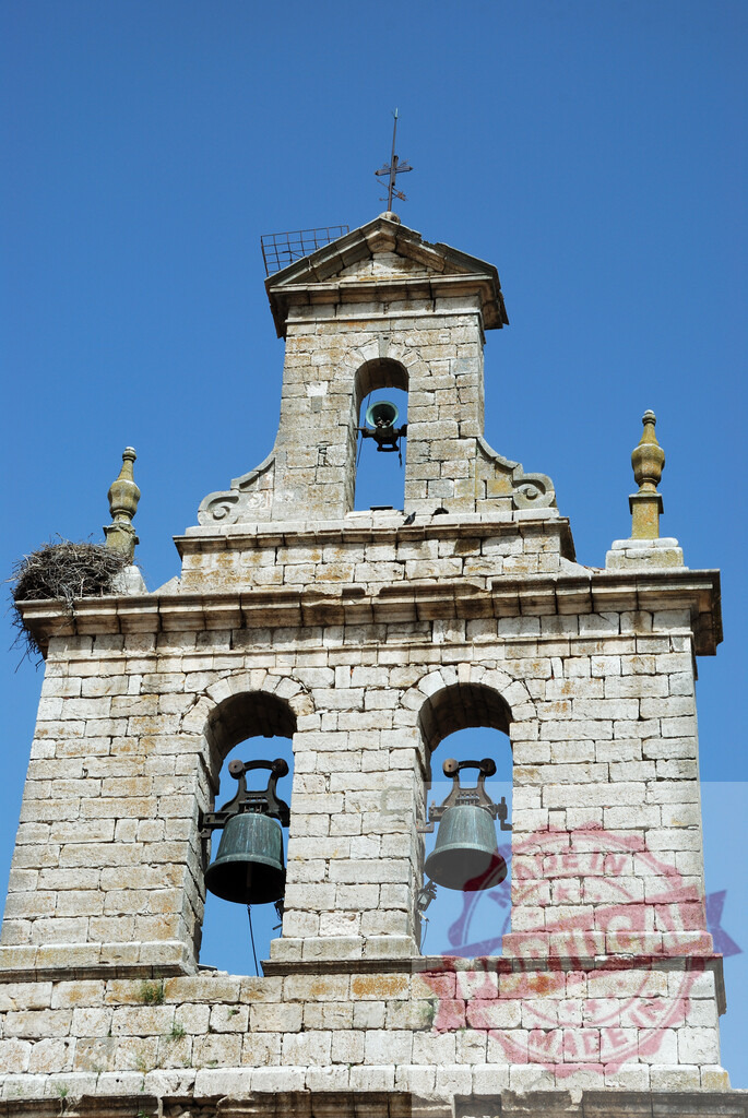 Church bell tower with storks nest under blue sky. Spain - Burgos | Stone bell tower displaying ancient bells and a large bird nest against clear blue sky - Realized with Pictrs.com