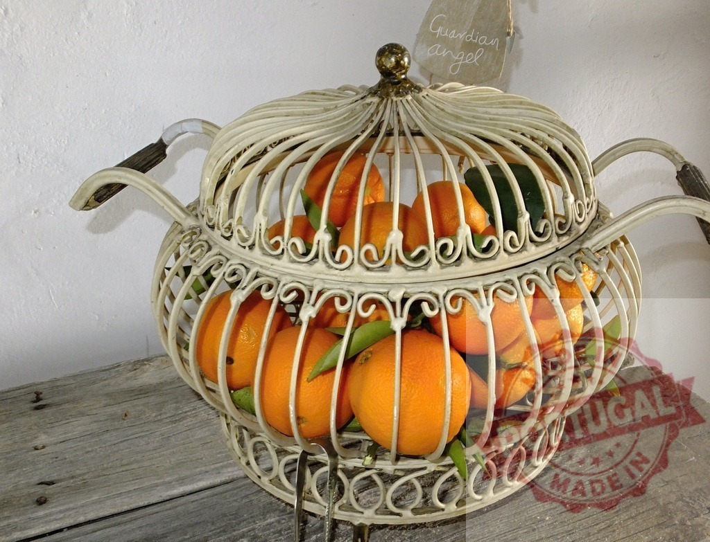 Oranges in vintage metal cage fruit basket on wood | Oranges with green leaves sitting inside an old metal cage basket on a rustic wooden table - Realisiert mit Pictrs.com