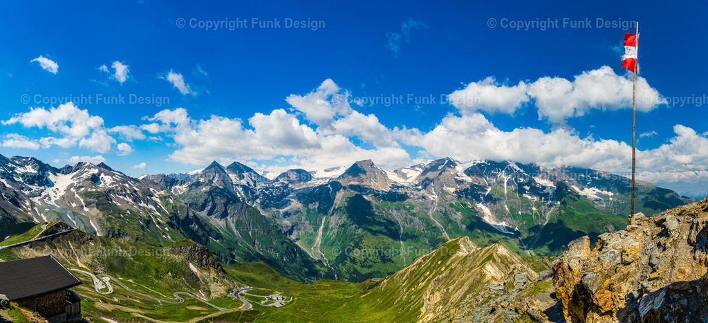 Panoramablick an der Großglockner Hochalpenstraße – Österreich | Ein weiter Panoramablick über die Alpen an der Großglockner Hochalpenstraße: schroffe Gipfel, helle Schneefelder und tiefgrüne Täler, darüber ein klarer Himmel mit dramatischen Wolken. Die österreichische Flagge am Fels setzt einen starken Akzent und macht das Motiv zu einem echten Statement für Bergliebhaber.