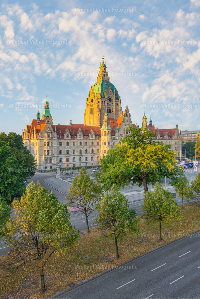 Neues Rathaus Hannover im ersten Licht | Das Neue Rathaus zeigt sich auf diesem Foto aus leicht schräger Perspektive, wodurch die monumentale Vorderseite besonders plastisch wirkt. Die frühe Morgensonne taucht die Sandsteinfassade in ein warmes, goldenes Licht und hebt die architektonischen Details klar hervor – von den Türmen bis zu den geschwungenen Giebeln. Ein Moment, in dem das historische Bauwerk nicht nur beleuchtet, sondern regelrecht inszeniert erscheint. - Realisiert mit Pictrs.com