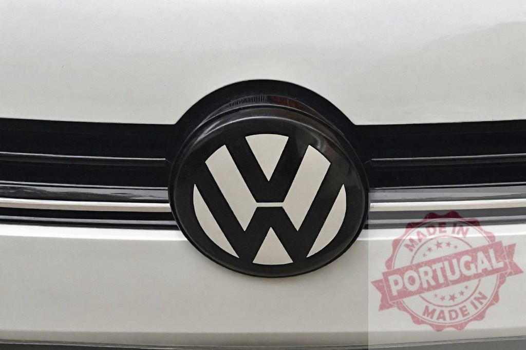 Volkswagen emblem badge on white car grille | Volkswagen logo on the front grille of a modern white car, showing automotive branding - Realisiert mit Pictrs.com