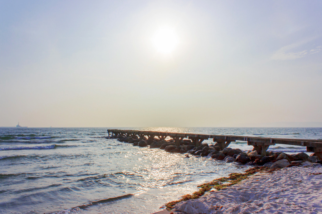 Wandbild: Seebrücke in schöner Morgenstimmung | Dieses Wandbild im Querformat zeigt eine Seebrücke in einer schönen Morgenstimmung. Der Himmel ist am Horizont noch leicht rötlich. Auf dem Meer gibt es zahlreiche Sonnenreflexionen.  - Realisiert mit Pictrs.com