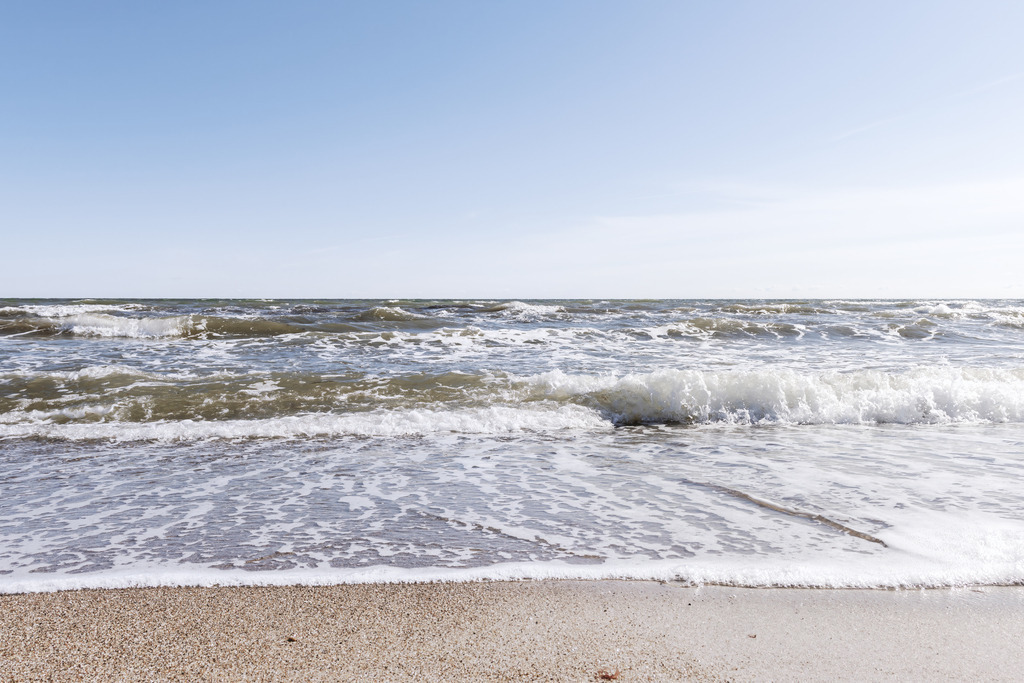 XXL Wandbild: Wellen am Ostseestrand | Maritime Dynamik und die Frische der Brandung im Querformat. Dieses XXL Wandbild fängt das lebendige Spiel der Ostsee ein: Weiße Gischtkronen brechen sich sanft und laufen in flachen, schäumenden Schleiern über den hellen Sandstrand aus. Der Blick reicht über die bewegte Wasseroberfläche bis zum weiten, klaren Horizont unter einem strahlend blauen Himmel. Holen Sie sich diese belebende Meeresbrise nach Hause, um in Ihren Wohn- oder Schlafräumen eine helle und vitale Atmosphäre zu schaffen. Die natürliche Farbkombination aus dem strahlenden Weiß der Gischt, dem tiefen Blau des Wassers und den warmen Tönen des Sandes verleiht jedem Raum eine spürbare Weite und maritime Frische.