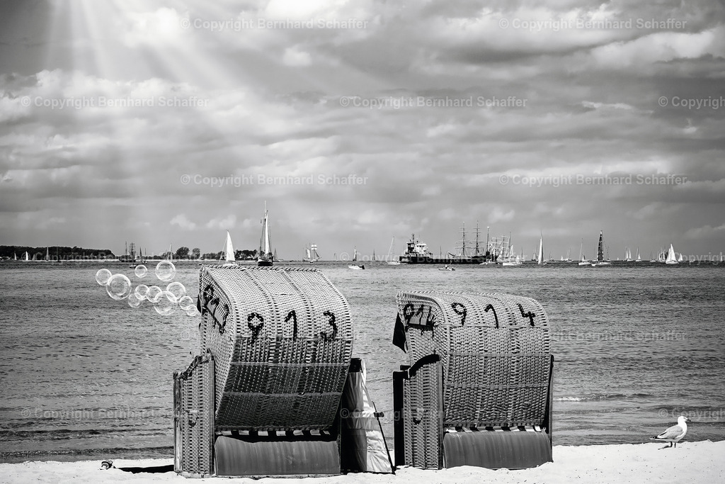 Typische Strandszene an der Ostsee | Zwei Strandkörbe an einem Sandstrand der Ostsee mit Seifenblasen und vielen Schiffen auf dem Meer am Horizont, schwarz-weiss. - Realisiert mit Pictrs.com