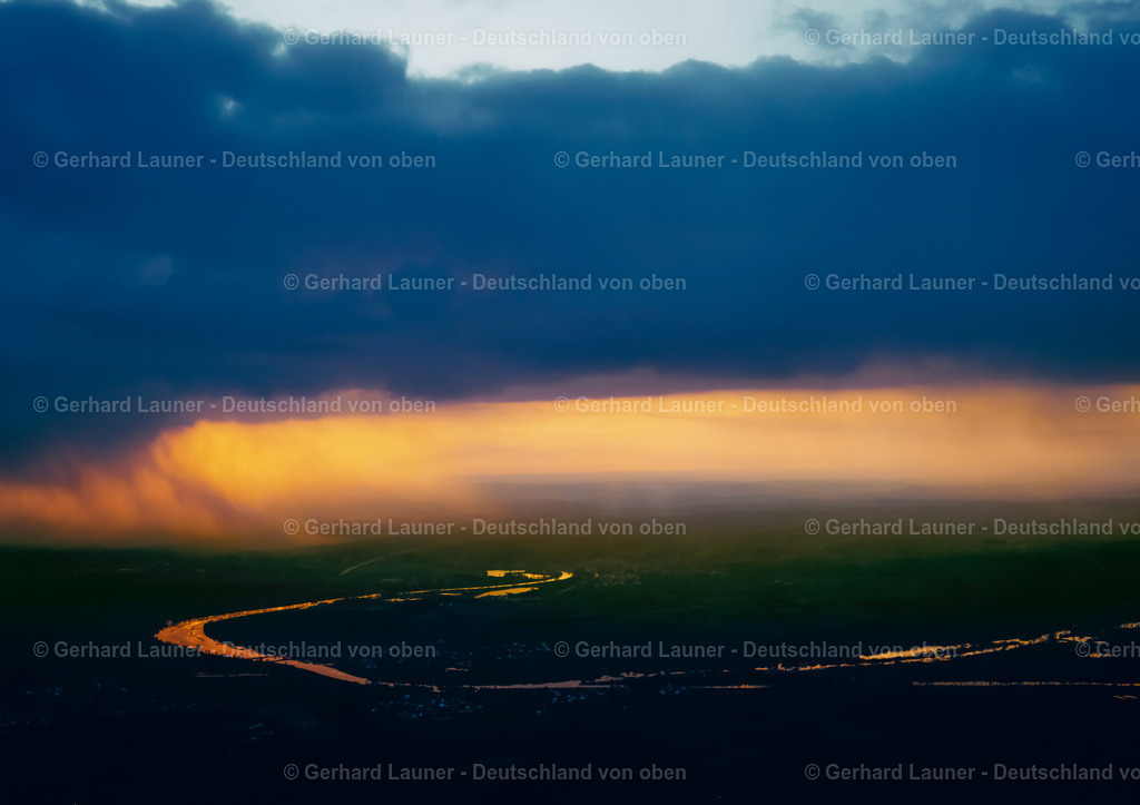 9100195 | Ein Regenschauer zieht gerade über Schwarzach am Main hinweg. Die tiefstehende Sonne lässt den Regen rötlich erscheinen.
