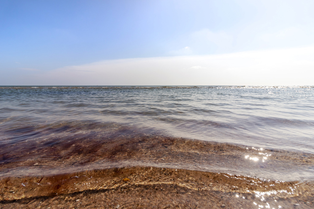 Wandbild: Glitzernde Küstenwellen | Dieses Wandbild im Querformat zeigt die Magie eines sonnigen Tages am Ostseestrand. Die sanften Wellen spiegeln das Sonnenlicht wider, während sie sich langsam an den Strand heranwagen. Ein wunderbares Stück, um die Natur und ihre Schönheit zu feiern. - Realisiert mit Pictrs.com