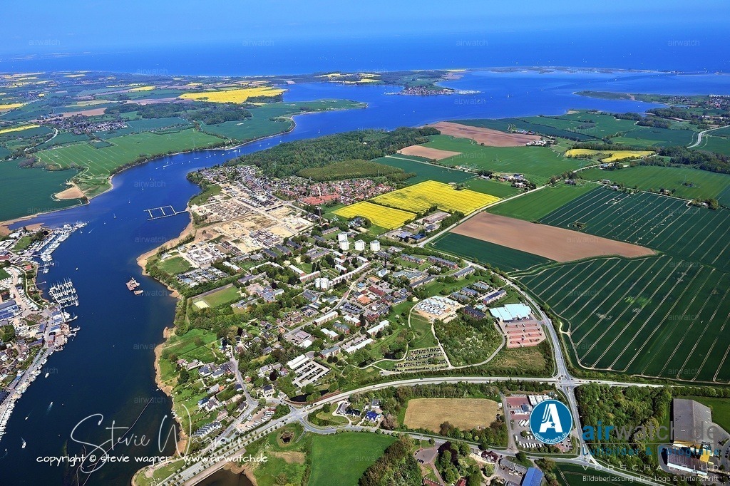 Luftbild Kappeln an der Schlei & Ellenberg | Kulinarisch lohnt sich ein Besuch bei Peter Jöhnk, der Fisch direkt vom Kutter verkauft – die Ware ist so frisch, dass man den Kutter noch tuckern hören kann. In Maasholm, einem Fischerdorf in der Nähe, kann man frischen Fisch in den lokalen Fischräuchereien probieren. Die Aal- und Fischräucherei Friedrich Föh thront mit ihren drei Schornsteinen über der Stadt und bietet traditionell geräucherte Spezialitäten. Für einen entspannten Nachmittag empfiehlt sich das Café Sandwig am Weidefelder Strand, das einen atemberaubenden Blick auf die Ostsee bietet