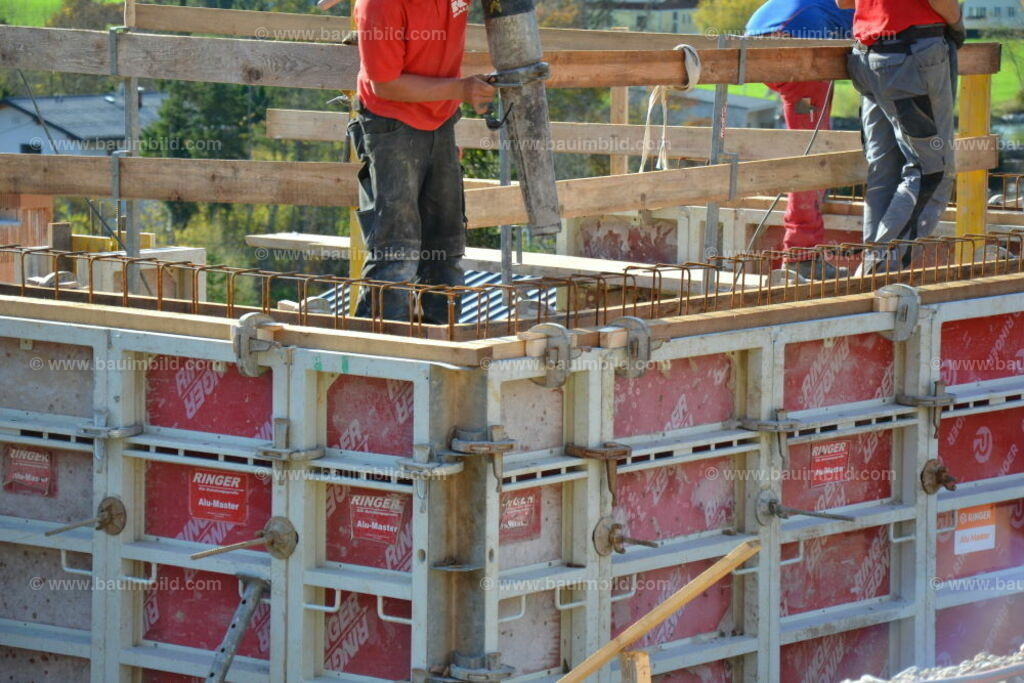 Betonwände betonieren | Auf Schutzgerüst stehender Arbeiter mit Endschlauch der Autobetonpumpe bereit zum Betonieren von geschalten und bewehrten Betonwänden