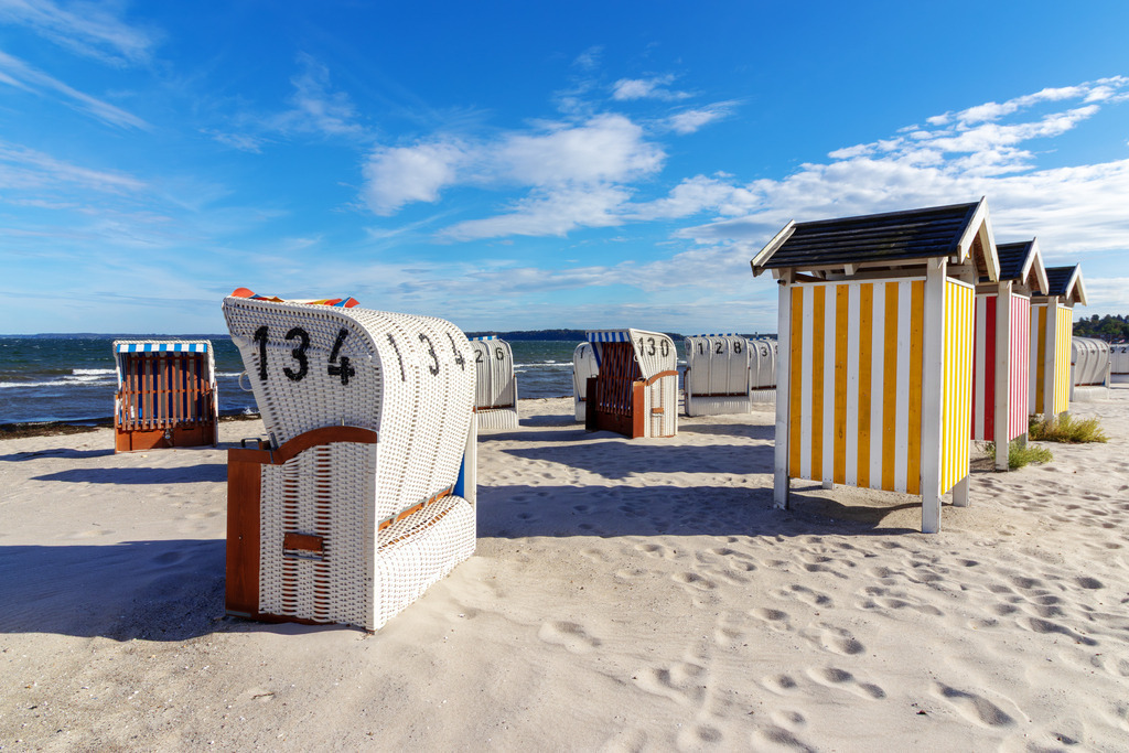 Wandbild: Strandtag in Eckernförde  | Dieses Wandbild zeigt eine typische Szene vom Strand in Eckernförde an der Ostsee. Im Vordergrund steht ein weißer Strandkorb, ausgerichtet zum Meer. Dahinter reihen sich farbenfrohe Umkleidekabinen mit gelb-weißen und rot-weißen Streifen entlang des Sandes – ein lebendiges Zeichen norddeutscher Strandkultur. Der Himmel ist weit und leicht bewölkt, das Wasser bewegt sich sanft im Hintergrund. Die Komposition lebt vom Zusammenspiel aus Farbe, Struktur und maritimer Atmosphäre – ein Bild, das Sommer, Ordnung und Entspannung zugleich vermittelt. Ideal als Wandbild für helle, naturnahe Wohnkonzepte – ob als Leinwandbild, Acrylglasbild, Alu-Dibond FineArt Print oder als Akustikbild. Ein frischer, fröhlicher Akzent für Wohnzimmer, Büro oder Ferienwohnung. - Realisiert mit Pictrs.com