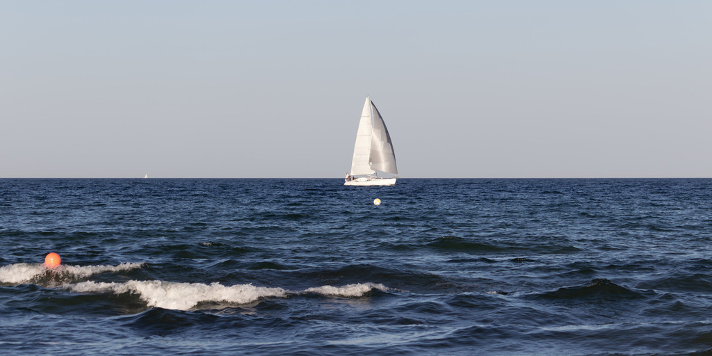 Panorama Wandbild: Segelboot auf der Ostsee | Dieses Panorama Wandbild zeigt ein Segelboot auf der Ostsee im Sommer. Im vorderen Bereich ist in der Unschärfe eine Welle mit Schaumkrone zu sehen. - Realisiert mit Pictrs.com