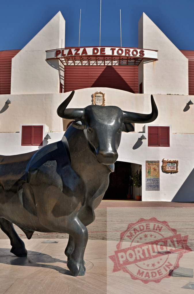Bull statue guarding historic Plaza de Toros arena | Bronze bull statue in front of a Spanish bullring, representing tradition and culture - Realisiert mit Pictrs.com