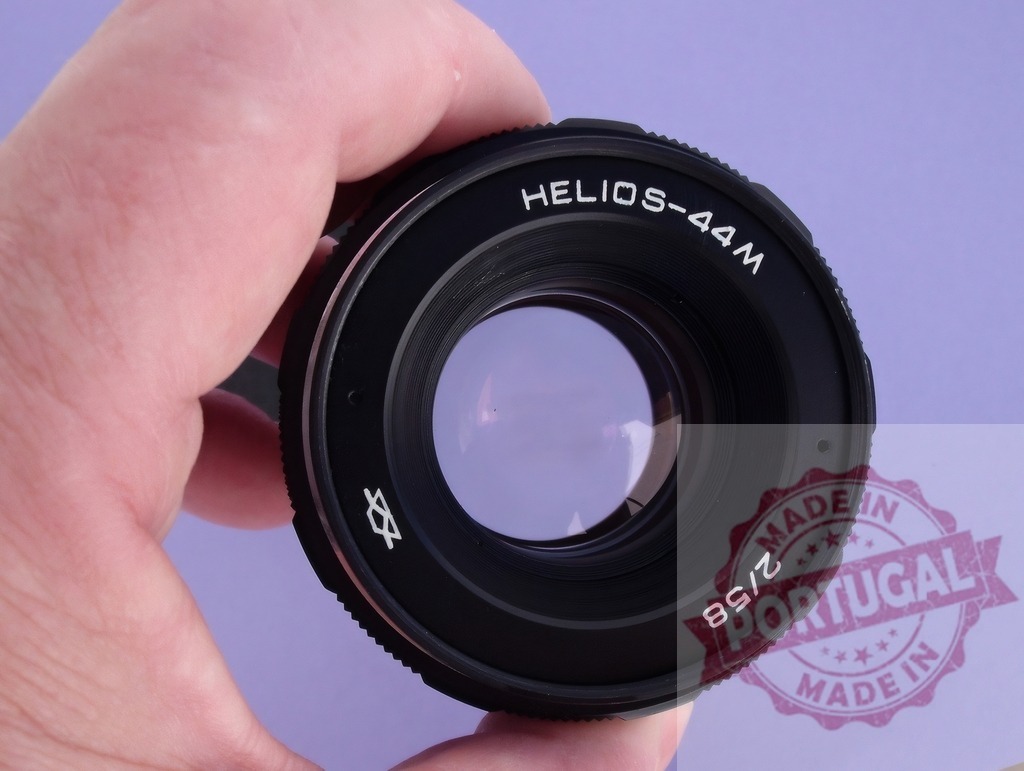 Hand holding vintage Helios-44M camera lens | Hand holding a black Helios-44M vintage camera lens against a purple background - Realized with Pictrs.com