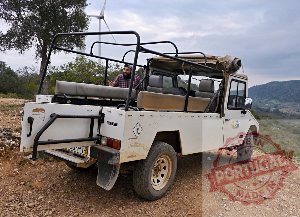 Safari vehicle on a dirt road by wind turbine | Off-road safari vehicle parked on a rural hilltop viewpoint with a man and wind turbine - Realized with Pictrs.com