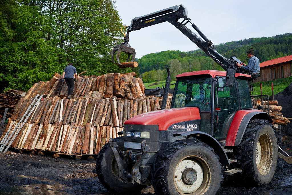 Waldköhlerei Hochecker | Michelbach, Austria - May 08, 2019: Waldköhlerei Hochecker, die 2011 in das Nationale Verzeichnis des immateriellen Kulturerbes der UNESCO aufgenommen wurde, produziert noch echte Holzkohle; roter Traktor mit Holzkran beim Aufbau des Kohlmeilers. - Realisiert mit Pictrs.com